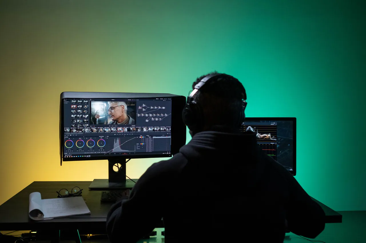 A creator editing video in a dark studio with timelines on the monitors